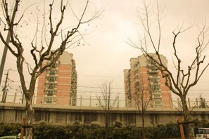 Un edificio de varios pisos con techo plano, rodeado de árboles sin hojas y un paso elevado de hormigón.