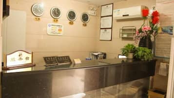 A reception desk with a clock, a bulletin board, and a potted plant.