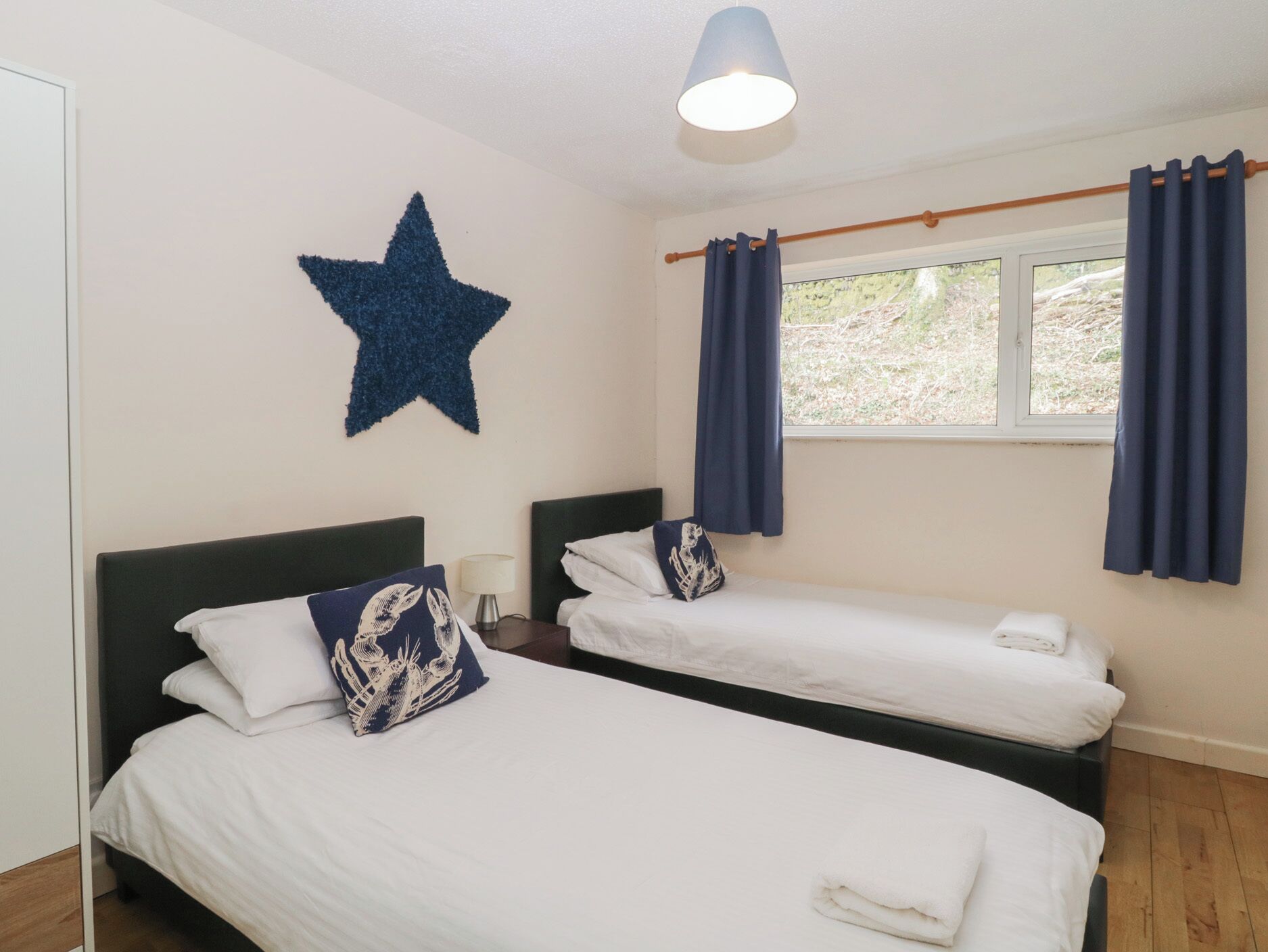 Une chambre d’hôtel avec deux lits, une décoration en forme d’étoile au mur, une fenêtre avec des rideaux et une lampe sur la table de chevet.