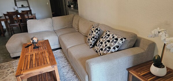 Un salón con un sofá modular, una mesa de centro de madera y una mesita auxiliar con una planta.