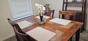A wooden dining table with placemats, chairs, and a vase of white flowers.