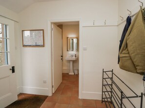 A hallway with a white door, a map on the wall, a bathroom with a sink and mirror, and a metal rack with clothes. - Winn's Cottage (Penrith)