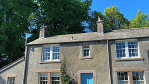 A two-story stone building with a blue door and windows, surrounded by greenery.