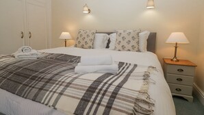A neatly made bed with a plaid blanket, two bedside lamps, and a small bedside table with a lamp.