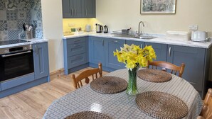A modern kitchen with grey cabinets, a built-in oven, and a dining area with a round table and woven placemats.