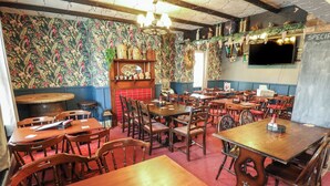 A restaurant with wooden tables and chairs, a floral wallpaper, and a bar area with bottles and glasses. - The Old Stables (Skegness)