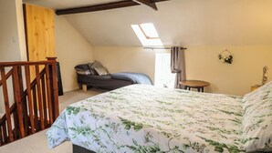 A bedroom with a bed, a wooden staircase, a skylight, and a small round table. - The Old Stables (Skegness)