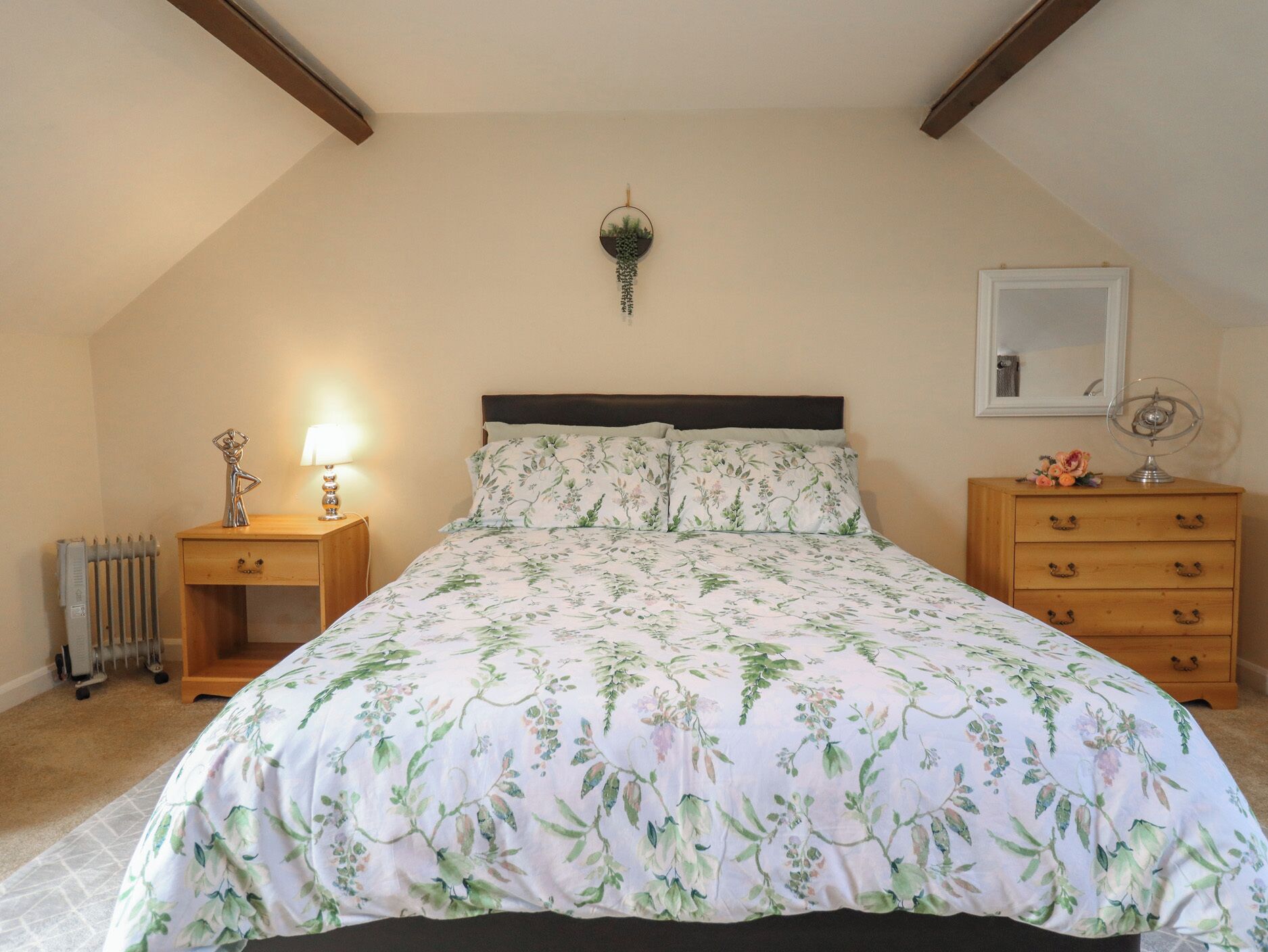 Um quarto com cama, mesa de cabeceira, cômoda, radiador e luminária na parede.