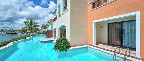 Une piscine à l’eau d’un bleu limpide, entourée d’un bâtiment doté d’un balcon et d’une grande fenêtre.