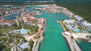 Ein Luftbild eines Küstenresorts mit einer Marina, Schwimmbecken und Unterkünften am Strand.