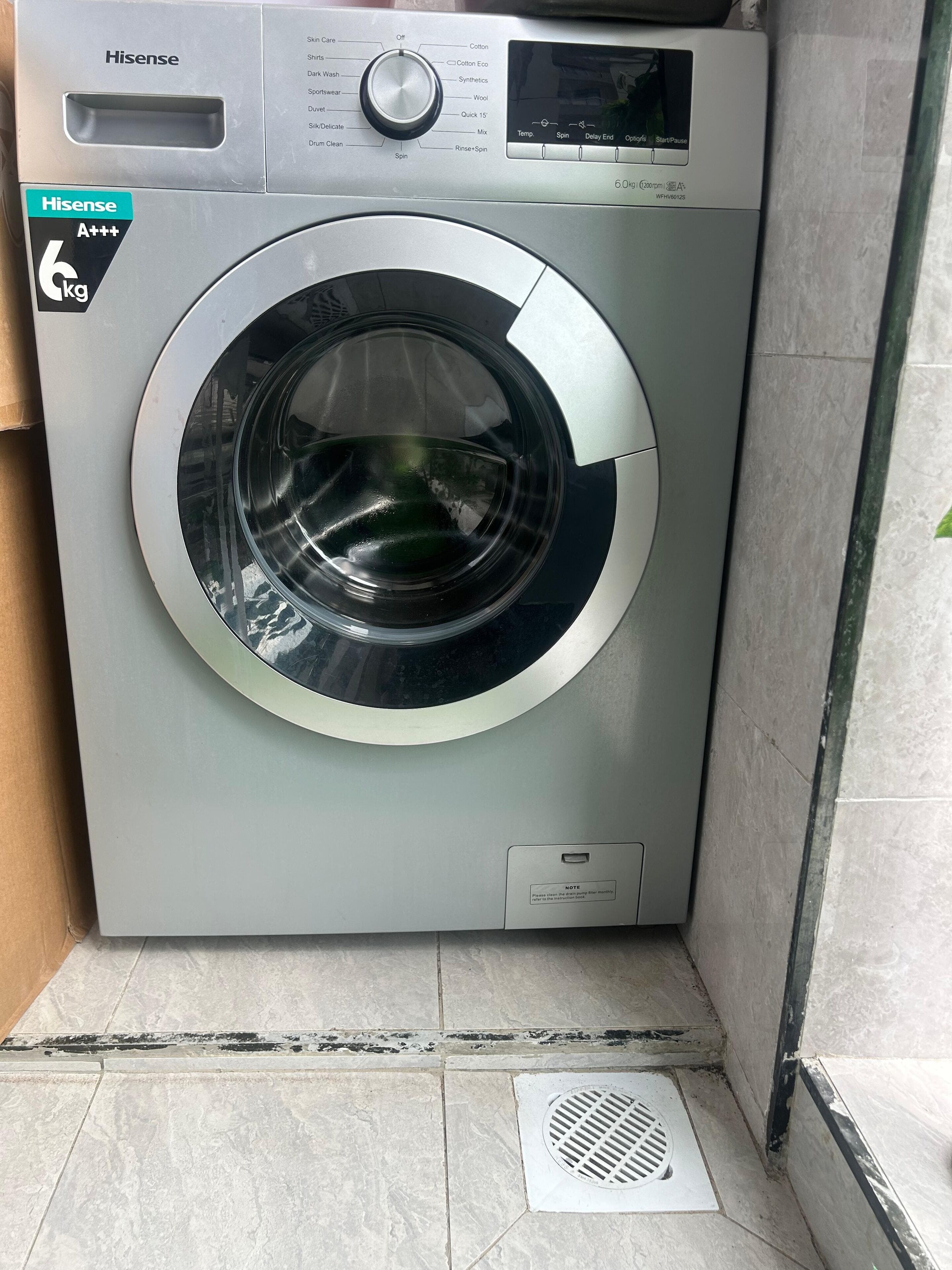 Una lavadora Hisense de carga frontal con panel de control, etiqueta que indica una capacidad de 6 kg y una nota sobre cerrar la puerta antes de iniciar el ciclo.