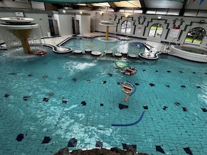 An indoor swimming pool with multiple lanes, a water slide, and a diving platform.