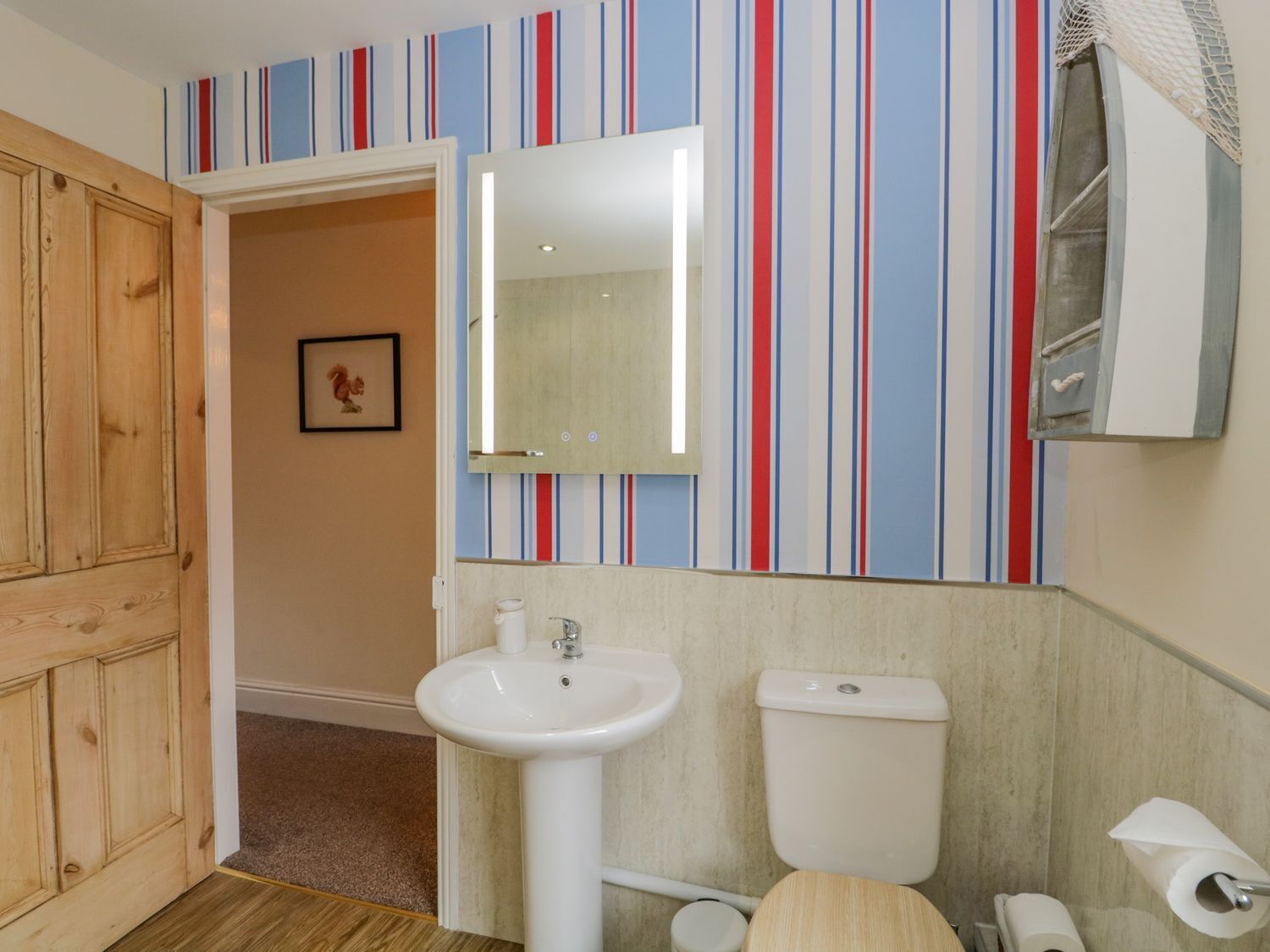 A bathroom with a wooden door, a white sink, a toilet, and a striped wall.