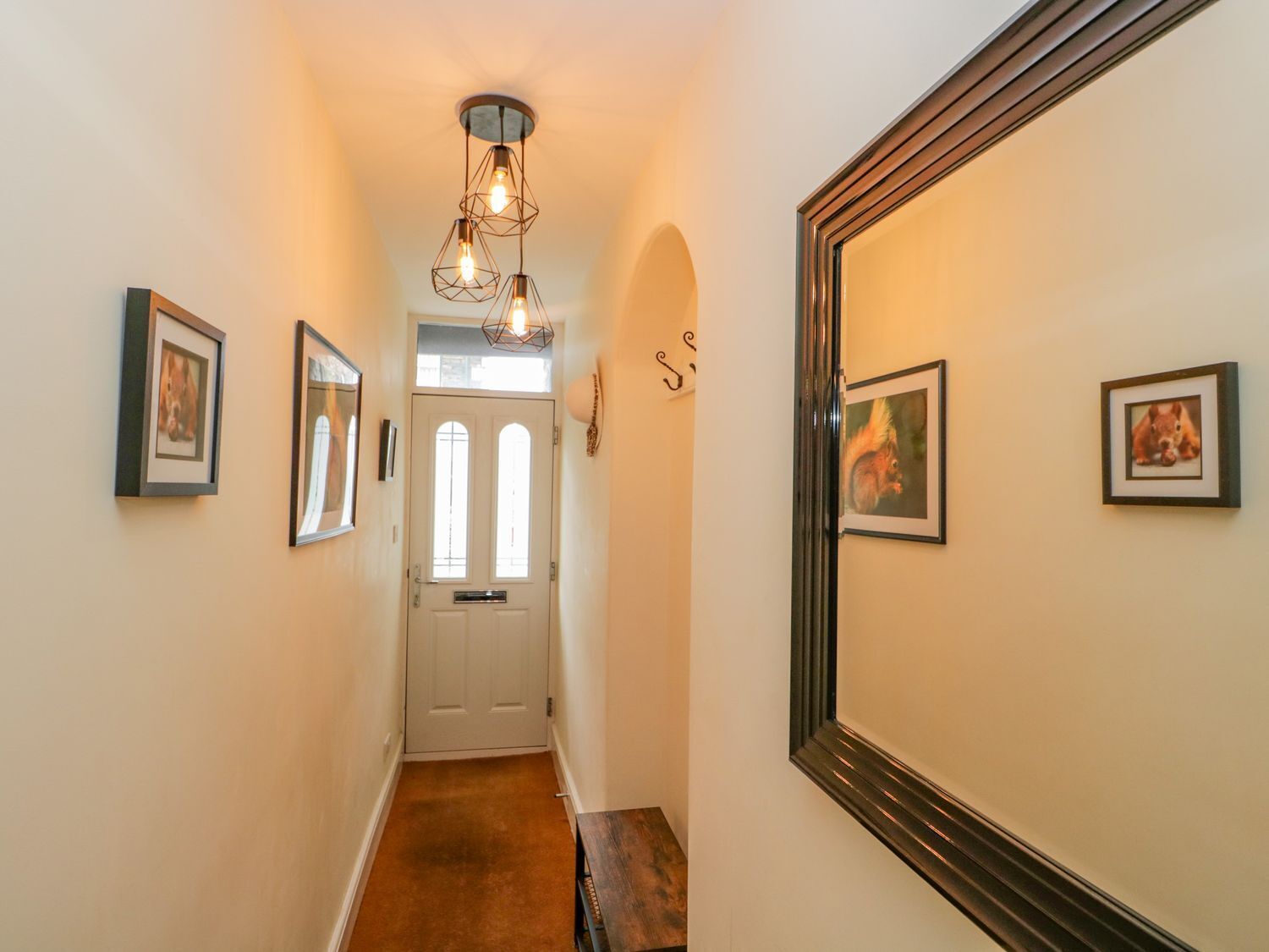 A hallway with framed pictures on the walls, a door at the end, and a light fixture above.