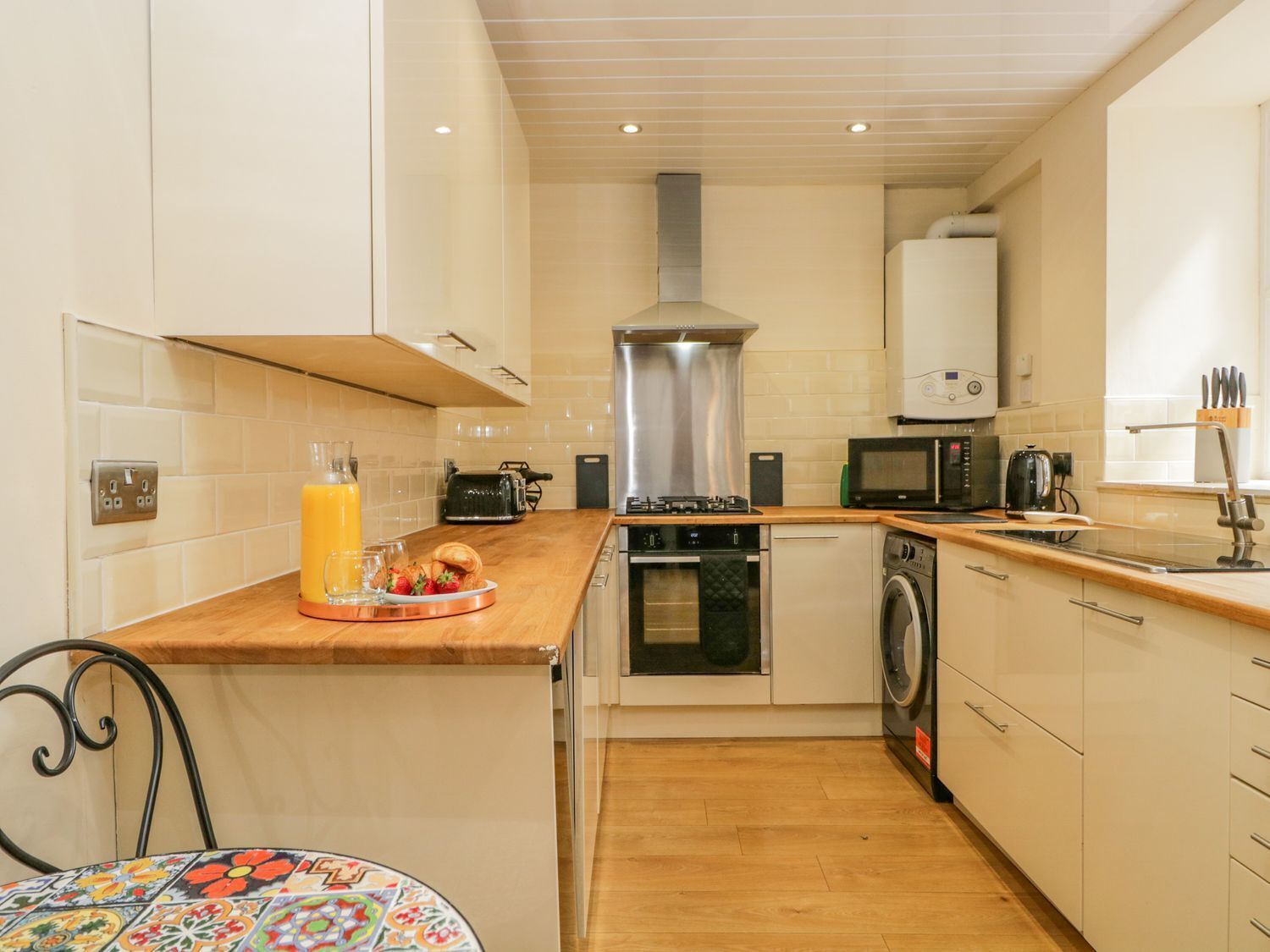 A compact kitchen with white cabinets, a wooden countertop, a built-in oven, a microwave, a toaster, and a sink.