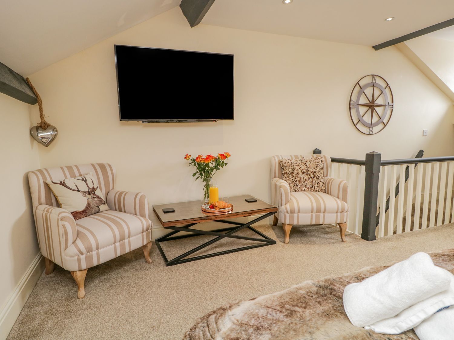 A living room with striped armchairs, a coffee table, a flat-screen TV, and a decorative compass on the wall.