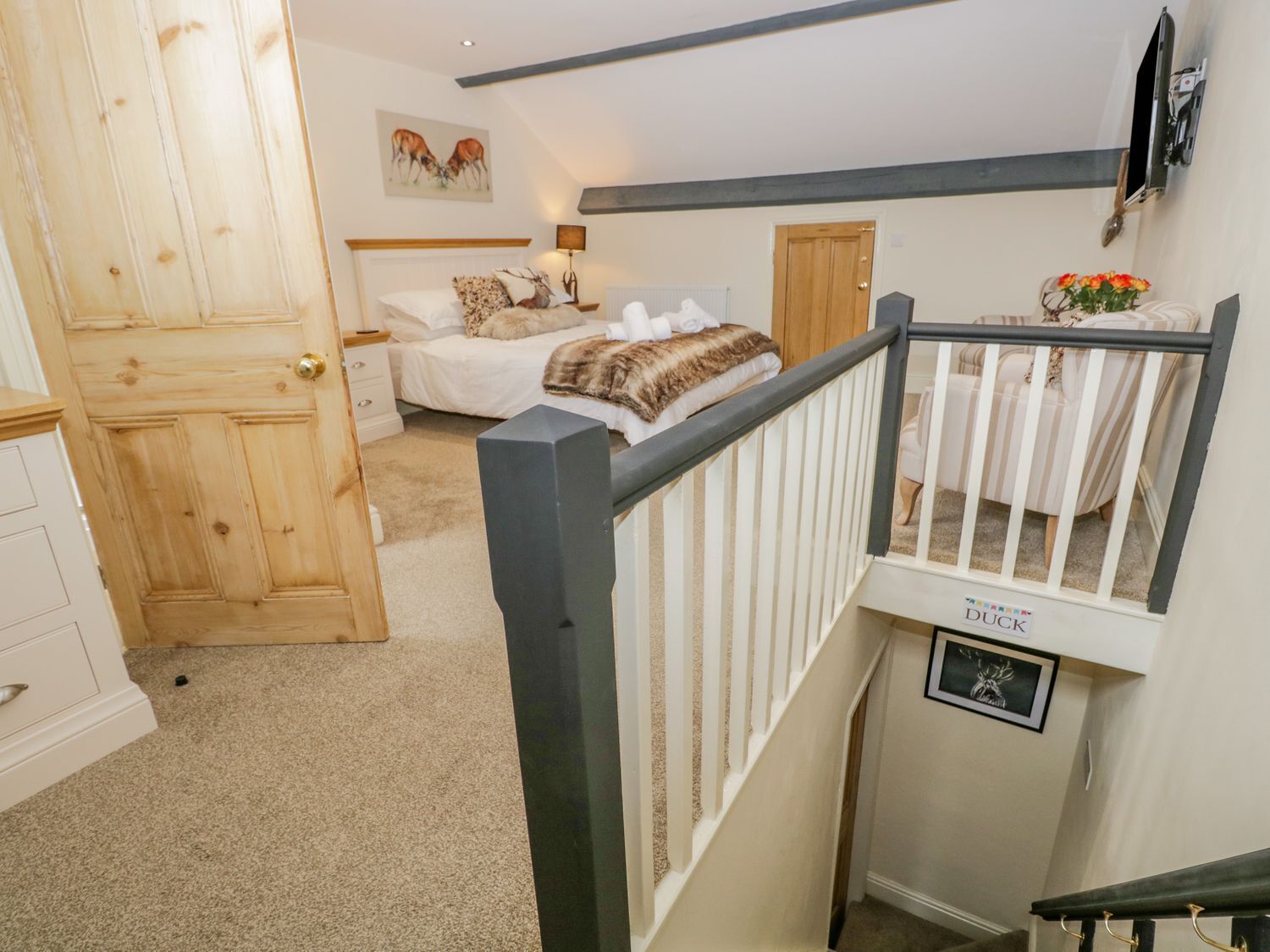 A bedroom with a bed, a wooden door, a white dresser, a painting on the wall, and a small white crib labeled "DUCK".