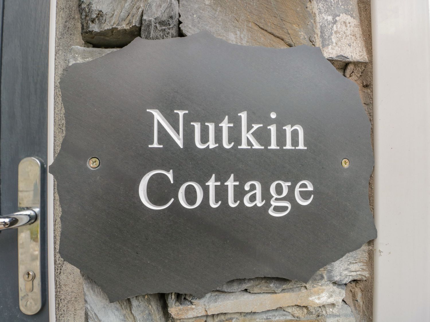 Un letrero de piedra con el texto "Nutkin Cottage" colocado sobre una pared de piedra.
