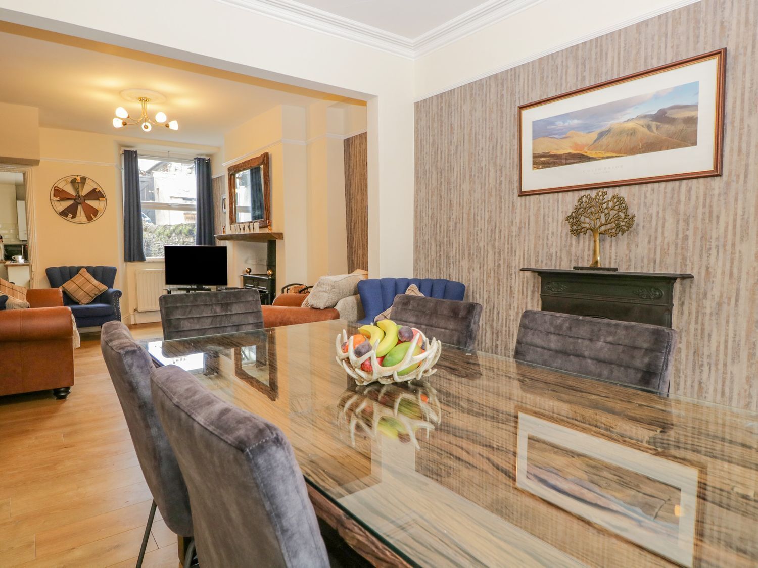 A spacious living room with a large glass table, comfortable seating, a fireplace, and a framed landscape painting.