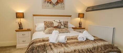A bedroom with a large bed, two bedside tables, a headboard, and a painting of deer on the wall.