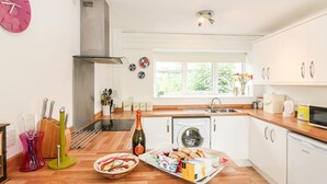 A modern kitchen with a built-in oven, a washing machine, and a large window providing natural light. - Tamar Cottages 35 (Gunnislake)