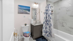 A bathroom with a toilet, sink, mirror, shower curtain, and bathtub.