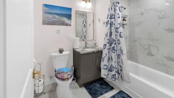 A bathroom with a toilet, sink, mirror, shower curtain, and bathtub.