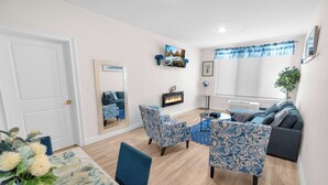 A living room with a fireplace, blue patterned furniture, a dining area with a table and chairs, and a large mirror.