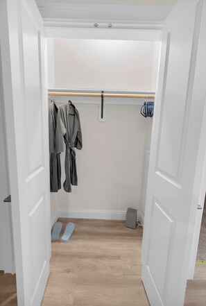 A walk-in closet with a wooden floor, a hanging rod, and a pair of slippers. - Blue Bliss 2BR 2BTH with FREE Parking, Near NYC & EWR Airport (East Orange)
