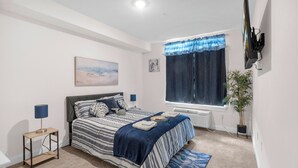 A bedroom with a bed, bedside tables, a window with curtains, a radiator, a plant, and artwork on the wall.