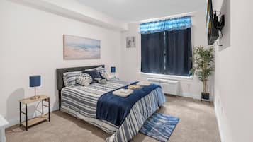 A bedroom with a bed, bedside tables, a window with curtains, a radiator, a plant, and artwork on the wall.