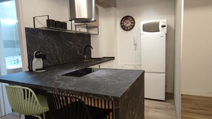 Una cocina moderna con encimera de mármol, estufa integrada, microondas y un reloj en la pared. Hay dos sillas y un ventanal grande.