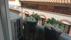 Un balcón con plantas en macetas y vistas a un edificio con tejados de tejas de arcilla y chimeneas.