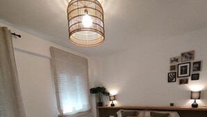 Un dormitorio con cama, mesita de noche con lámpara, ventana con cortinas y decoración en la pared.