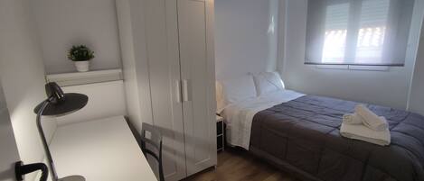 A bedroom with a bed, a desk, a chair, a wardrobe, and a hanging light fixture.