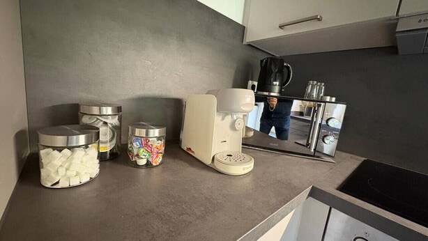 A modern kitchen with stainless steel appliances, including a coffee maker, a kettle, and a stove. There are containers with food items on the counter. - Forest View - near Rußweiher (Eschenbach in der Oberpfalz)