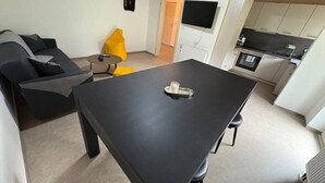 A modern living room with a black dining table, a sofa, and a kitchen area with white cabinets and a black countertop. - Forest View - near Rußweiher (Eschenbach in der Oberpfalz)