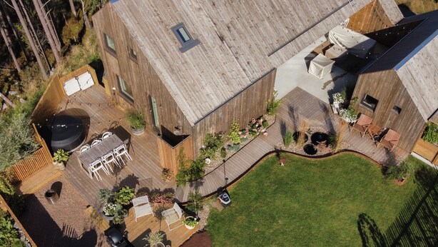 An aerial view of a modern building with a wooden deck, outdoor seating, and a landscaped garden.