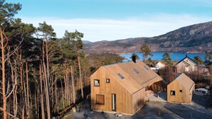 A wooden cabin with a large window and a door, surrounded by trees and a lake.