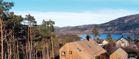 Une cabane en bois dotée d’une grande fenêtre et d’une porte, entourée d’arbres et bordée par un lac.