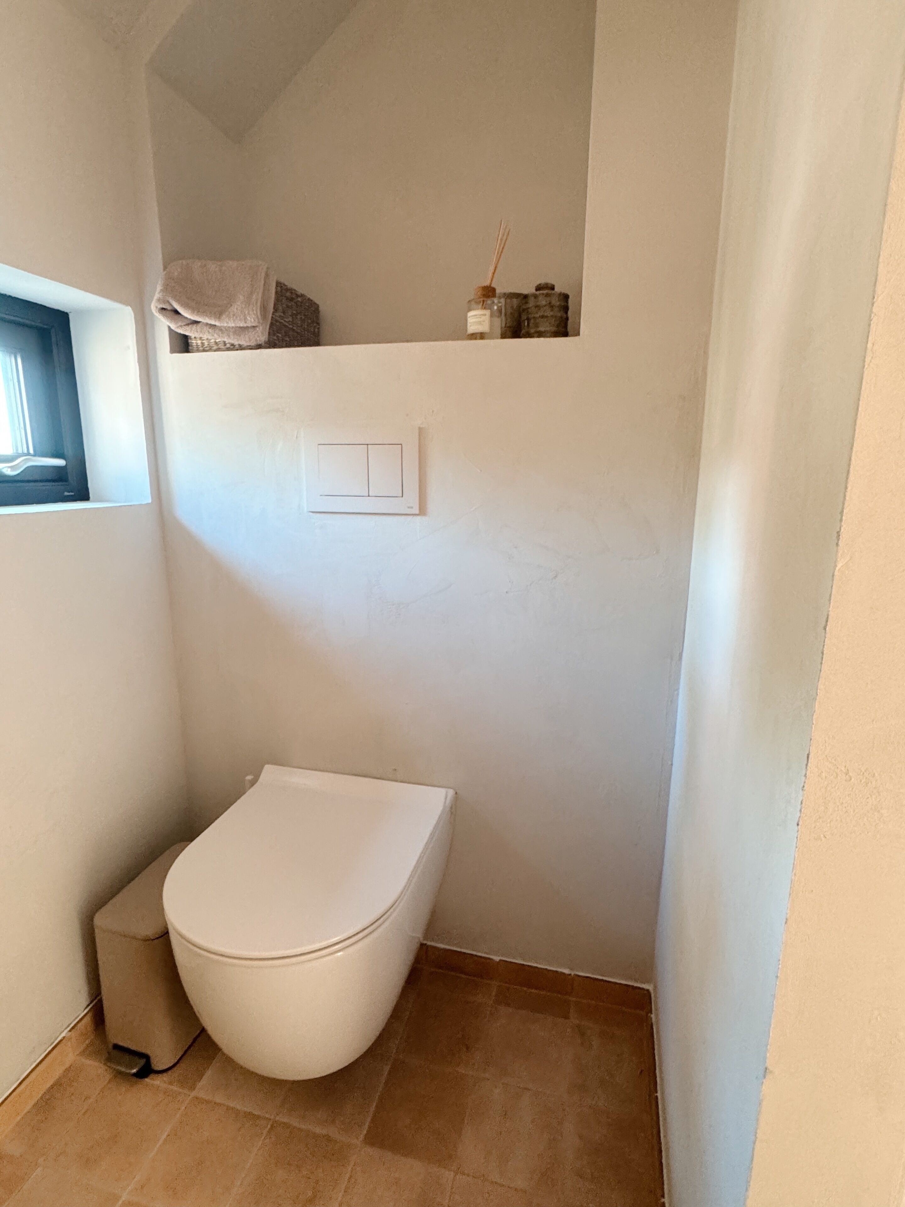 Ein kleines, weißes Badezimmer mit Toilette, Handtuchhalter und Fenster.
