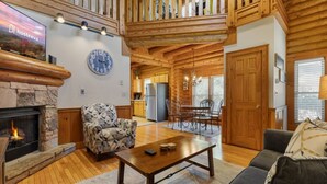 L’intérieur d’une cabane en rondins, avec une cheminée en pierre, un coin repas et un salon comprenant un canapé et une table basse.