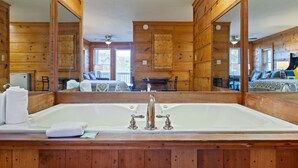 A wooden cabin with a large mirror above a bathtub, wooden walls, and a visible kitchen area. - Suite at Dollywood Lane (Pigeon Forge)