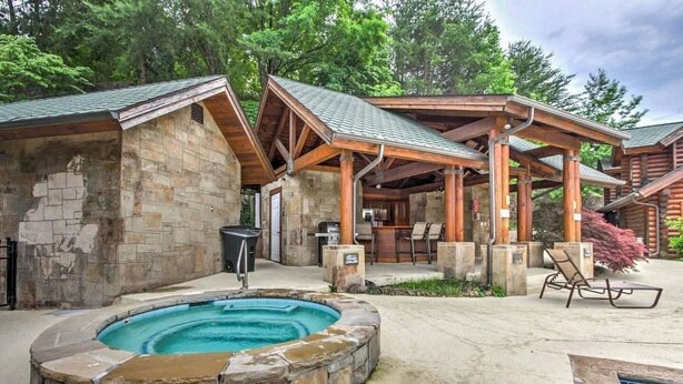 A rustic cabin with a stone exterior, a hot tub, and outdoor seating areas. - Suite at Dollywood Lane (Pigeon Forge)
