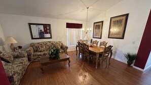 A living room with a sofa, coffee table, dining table with chairs, a chandelier, and framed artwork on the walls. - Luxury Vacation Home in Kissimmee, Perfect for Families and Golfers (Kissimmee)