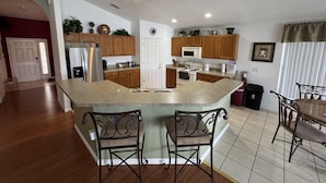 A modern kitchen with wooden cabinets, a central island with bar stools, and a dining area with a table and chairs. - Luxury Vacation Home in Kissimmee, Perfect for Families and Golfers (Kissimmee)