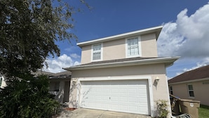 A two-story house with a white garage door, a small front yard, and a tree to the left. - Luxury Vacation Home in Kissimmee, Perfect for Families and Golfers (Kissimmee)