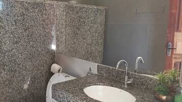 Un baño con encimera de granito, lavamanos blanco, inodoro y espejo.