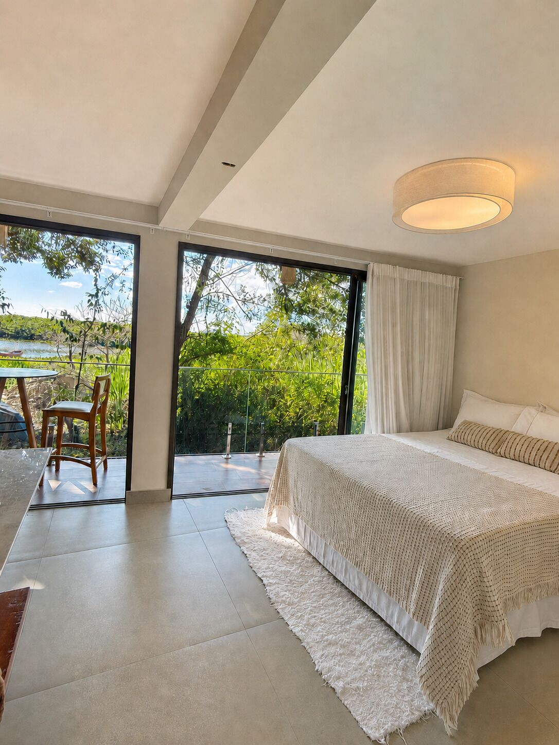 A modern bedroom with a large bed, a view of greenery, and a dining area with a table and chairs.