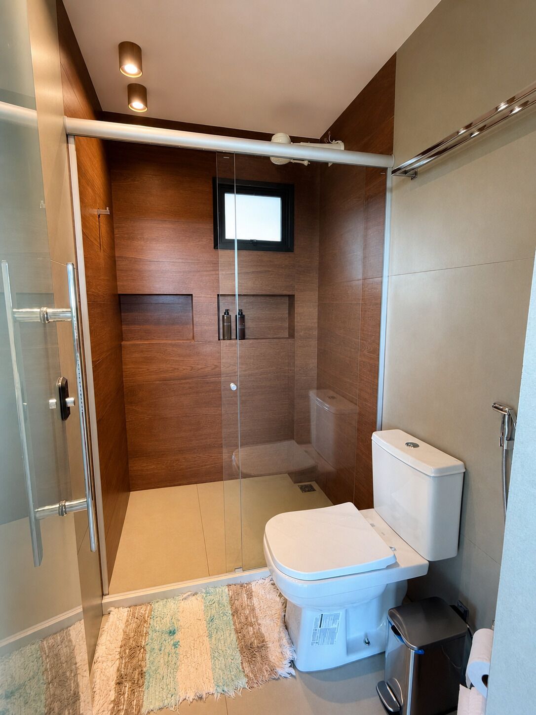 A modern bathroom with a glass shower enclosure, a toilet, and a small trash bin.